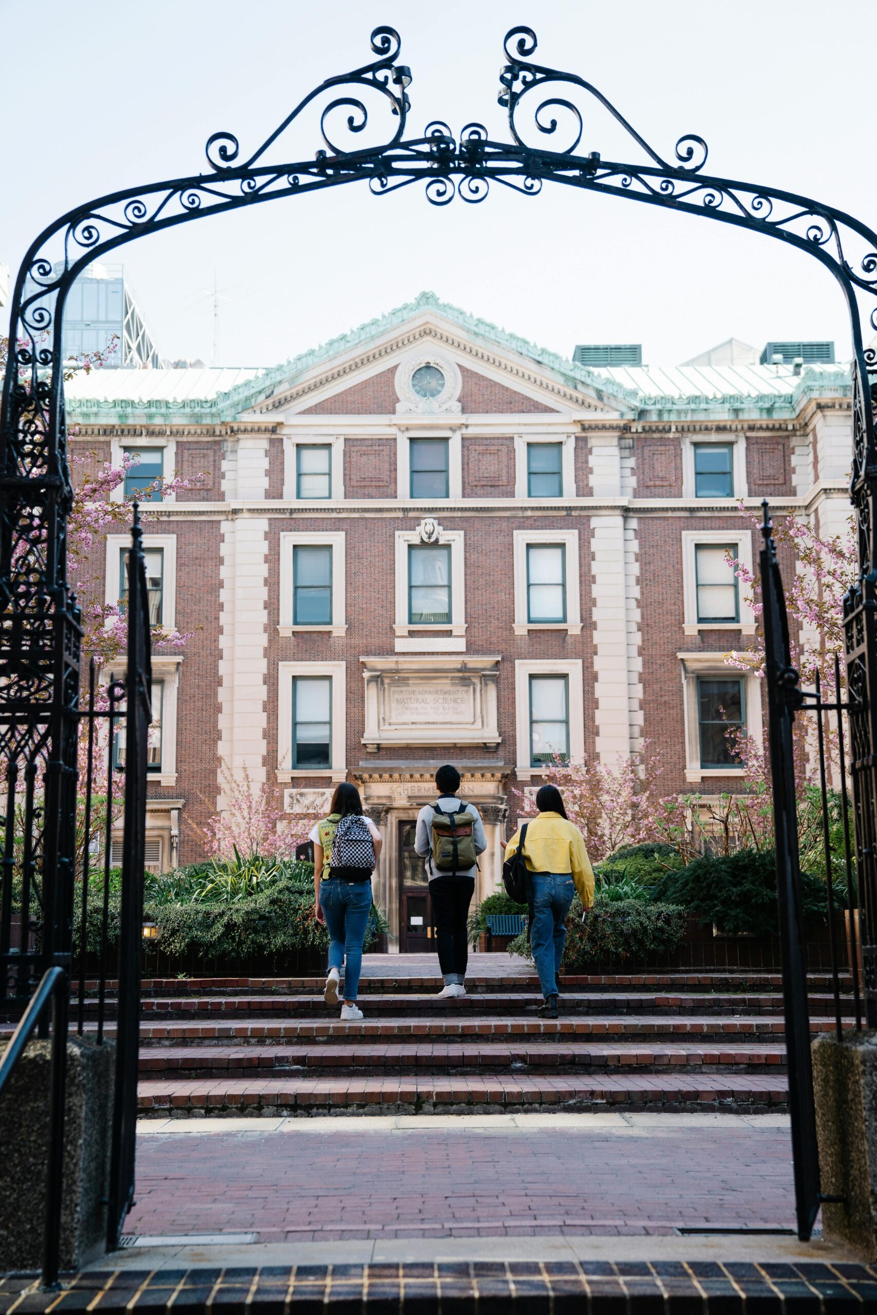 Three students walk through an archway towards a historic university building on campus.